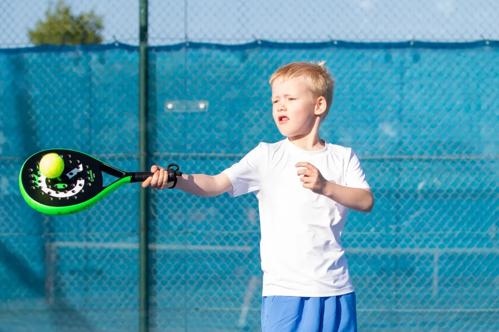Blonder Junge mit grünem Q Padel Kinderschläger