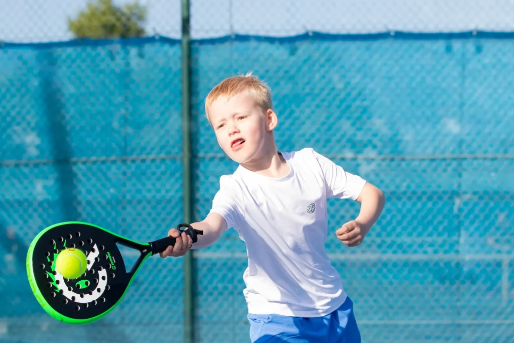 Blonder Junge spielt mit grünem Q Padel Kinderschläger